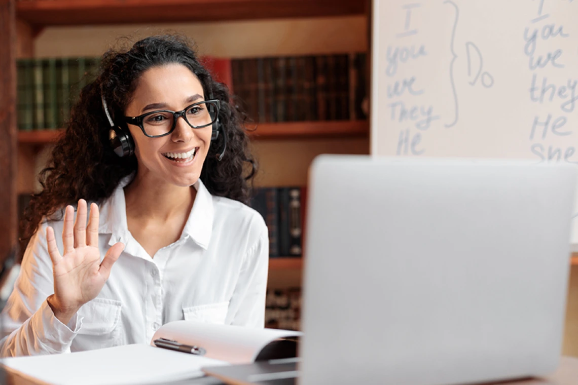 Person wearing headphones smiling and waving at laptop