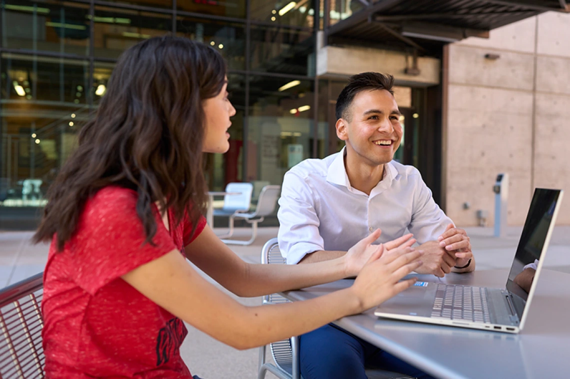 Two students sitting outside on a laptop having a conversation