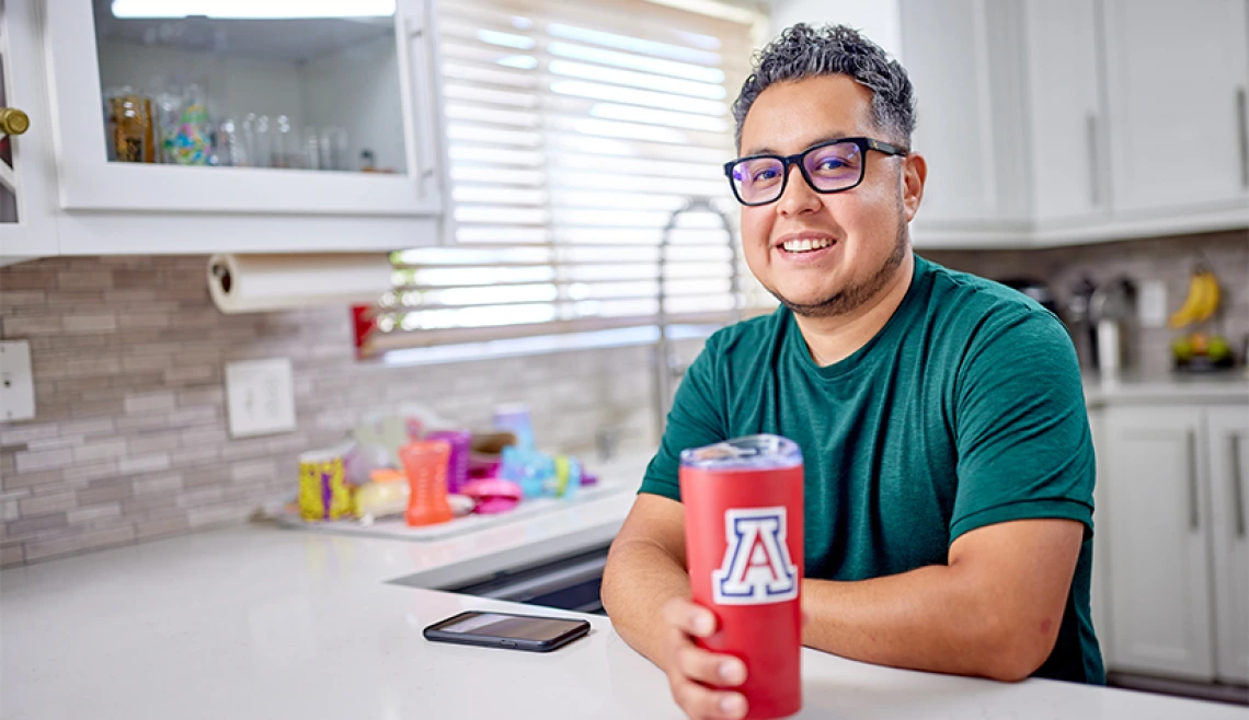 Person standing in home kitchen while holding a UA branded coffee mug