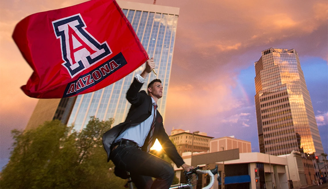Student riding on bike and holding up UA flag
